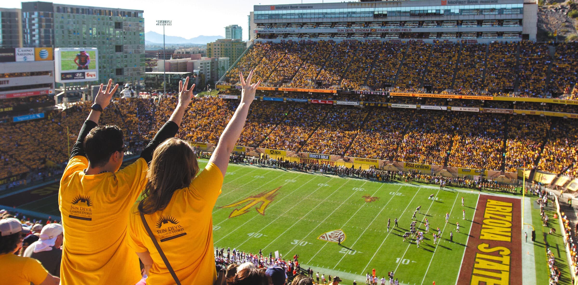 Two football fans, pictured from the back, in a packed Arizona State University stadium.