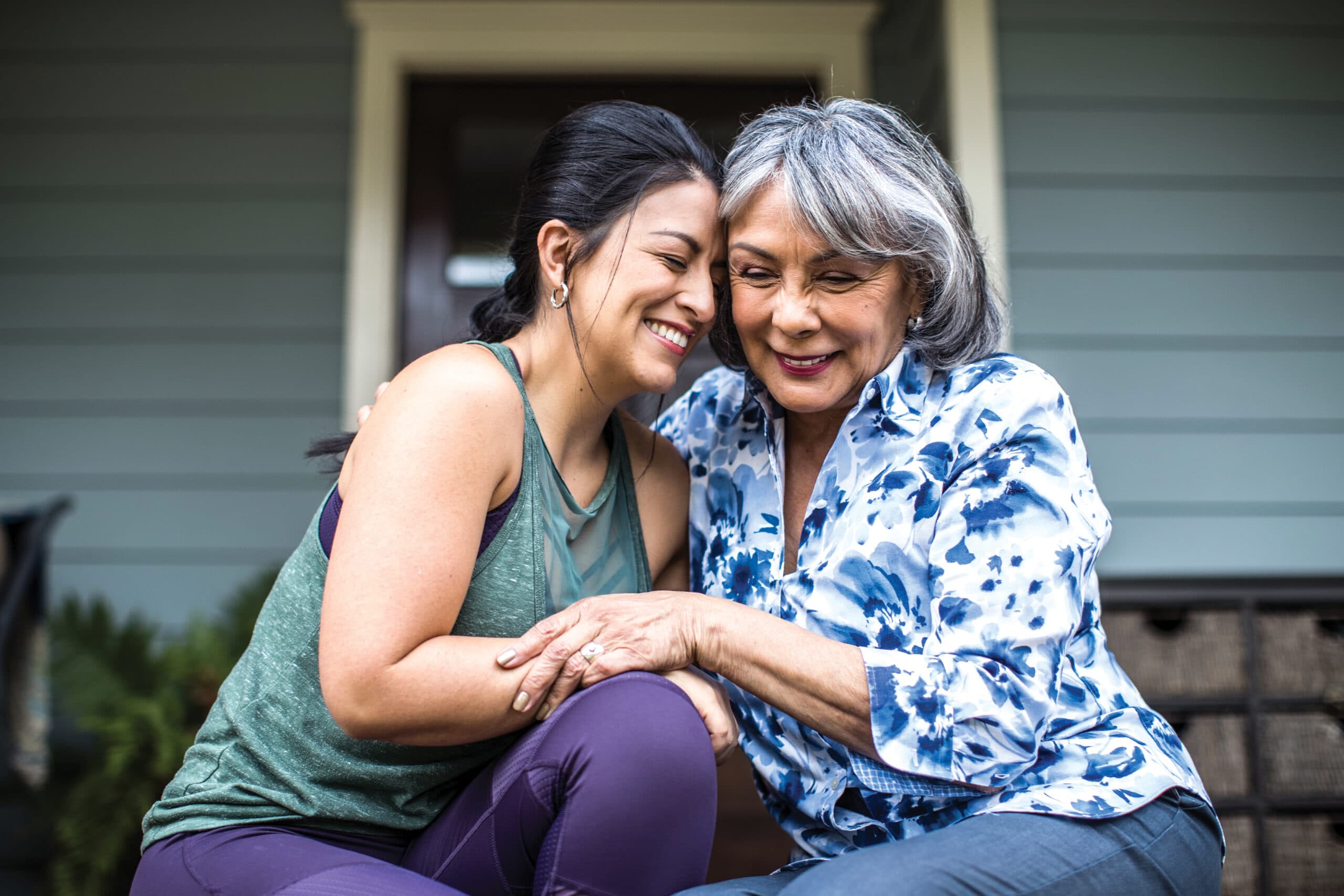 Senior woman and adult daughter laughing on porch.